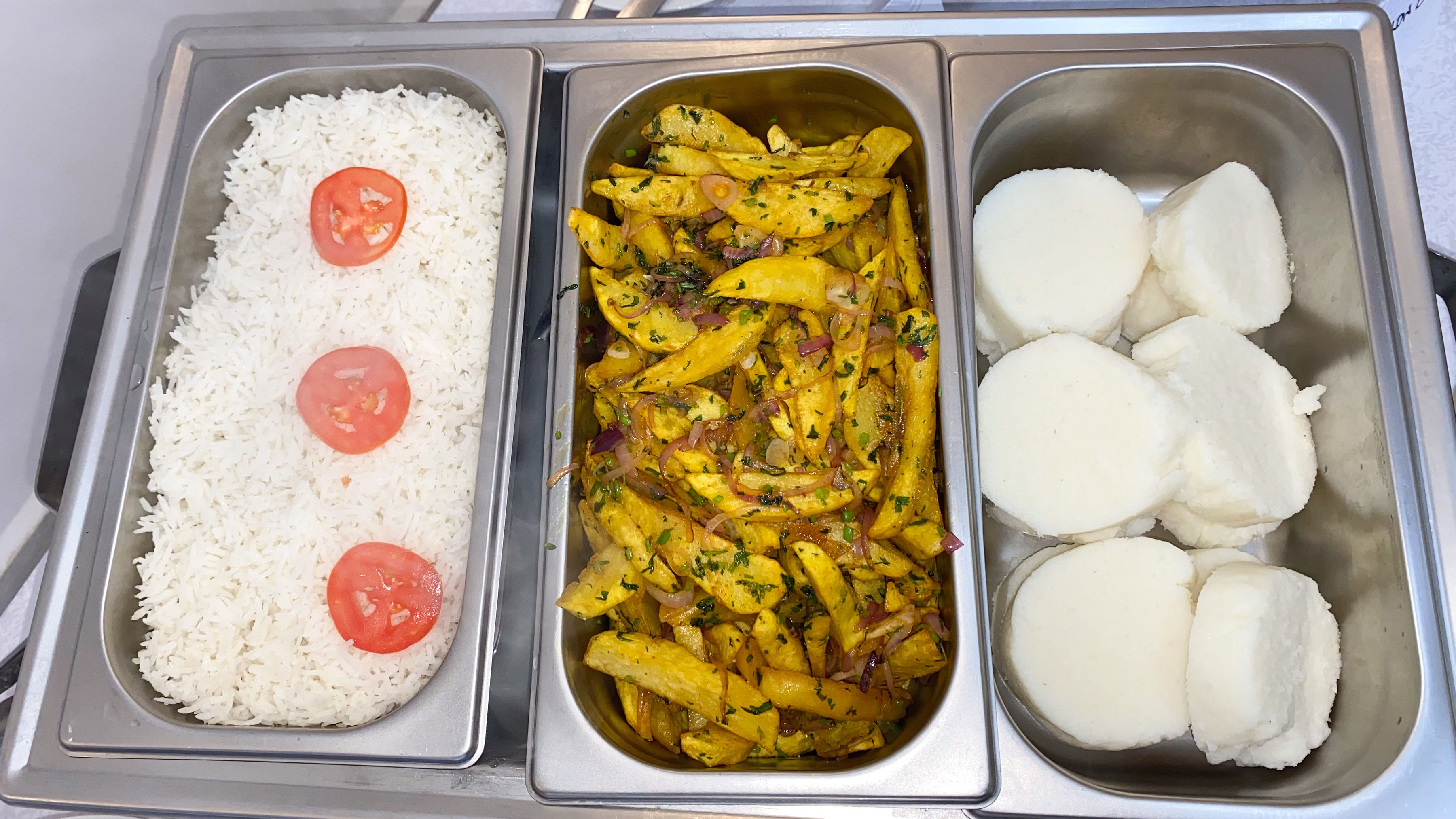 Buffet trays of rice garnished with tomato, seasoned potato wedges and ugali rounds