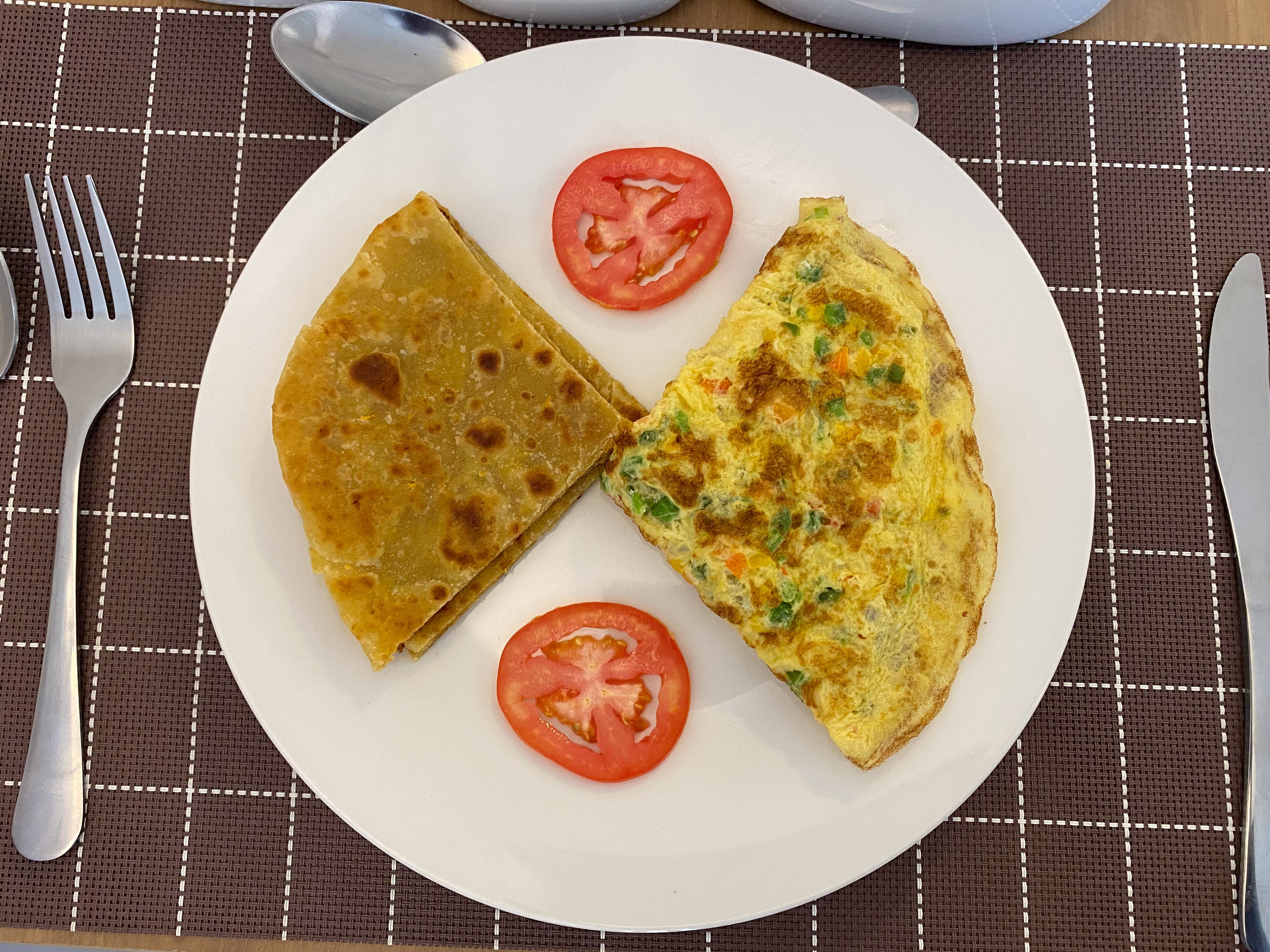 A herb omelette, folded chapati and tomato slices on a white breakfast plate