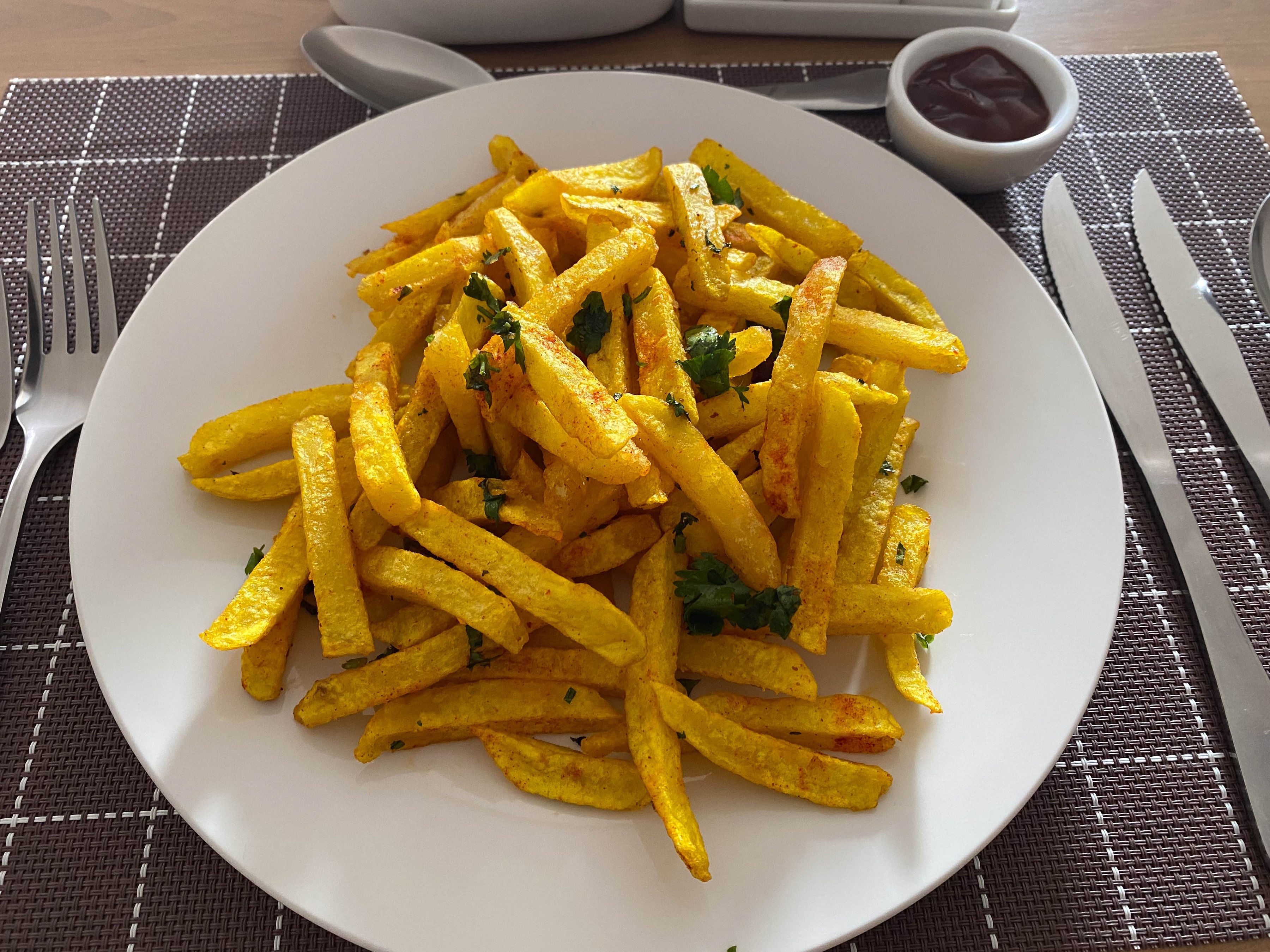 Seasoned golden fries with herbs on a white plate beside a bowl of sauce