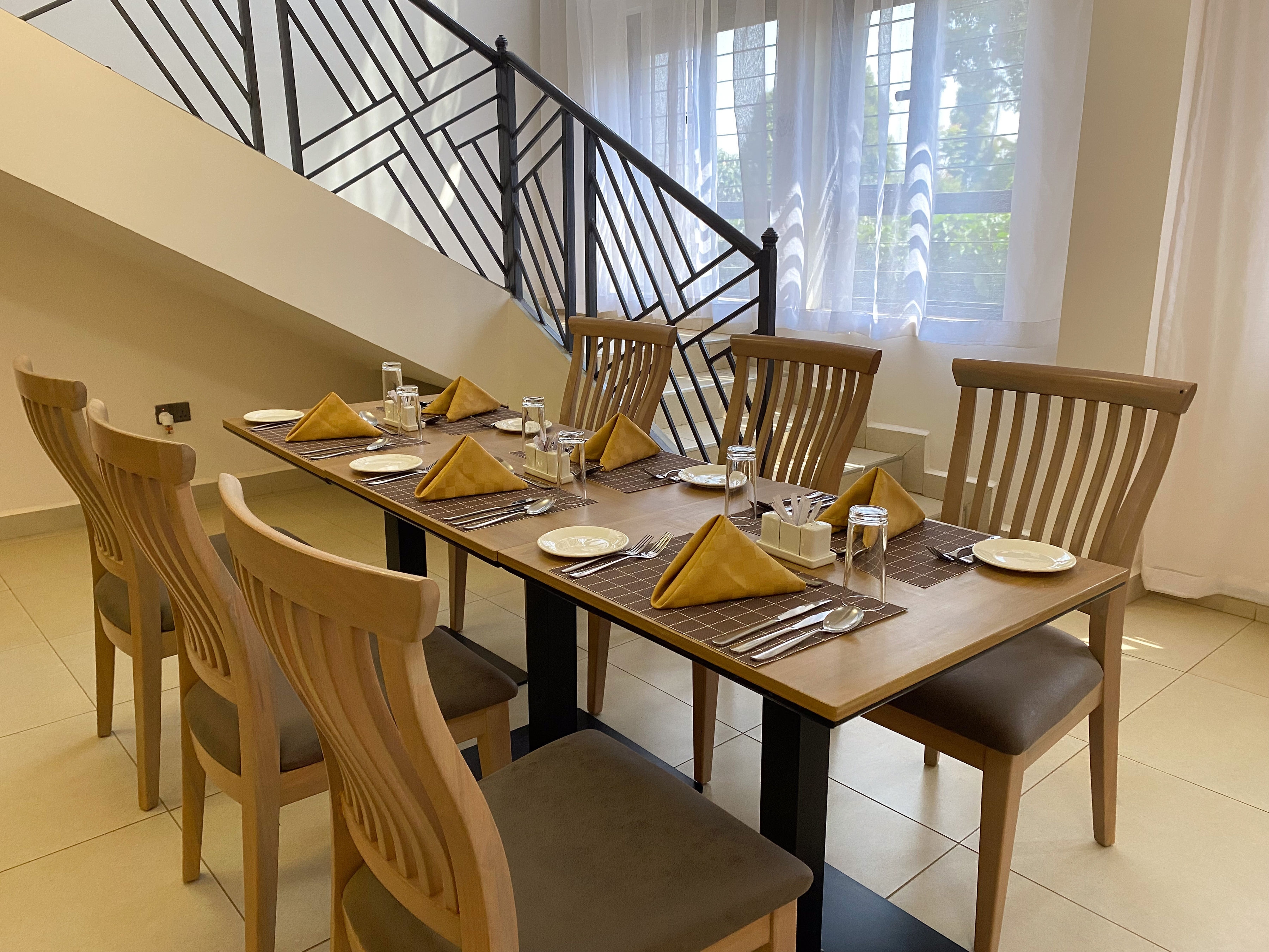 Wooden dining chairs around tables set with gold napkins beside the staircase and sheer curtains