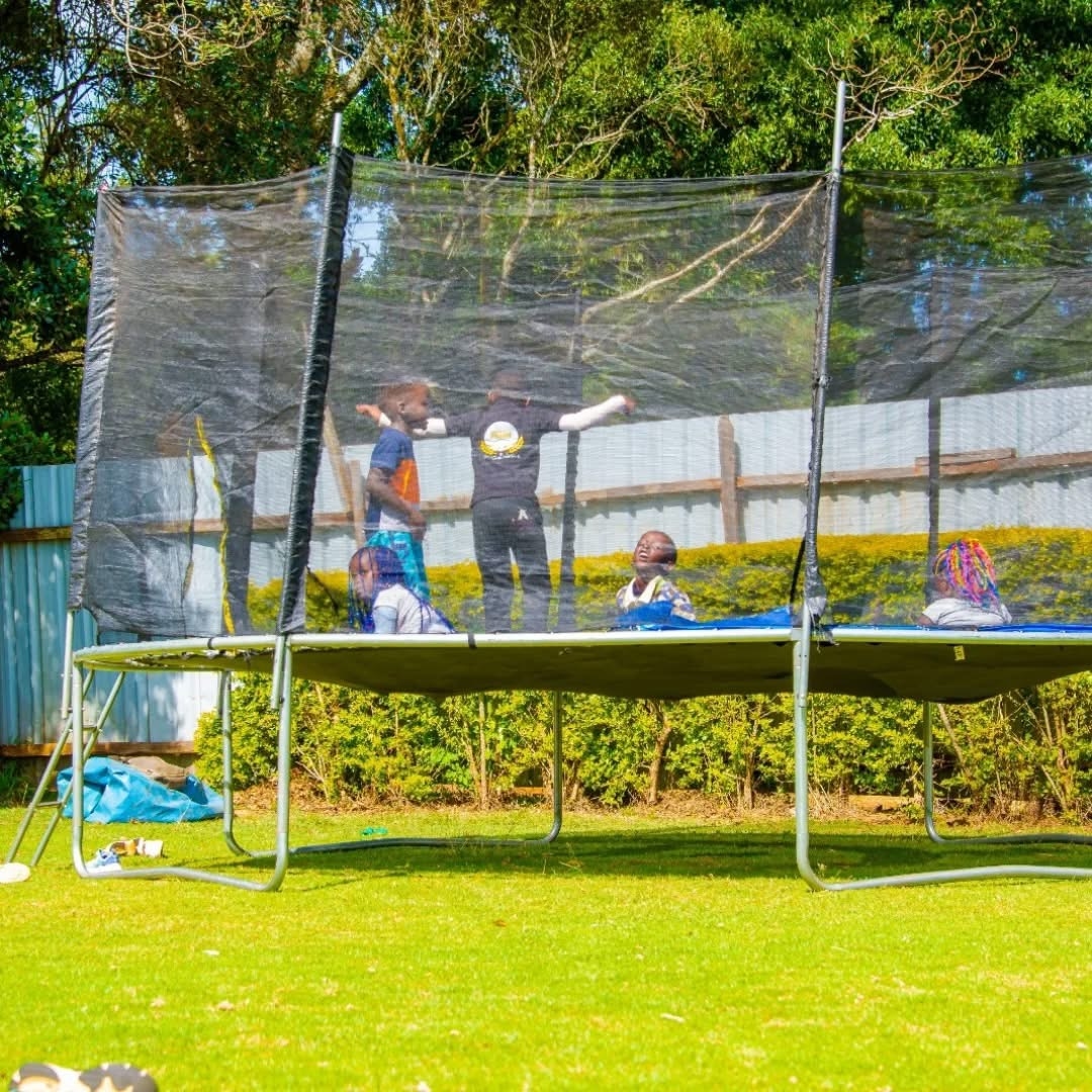 Children bouncing on a netted trampoline at the edge of the lawn