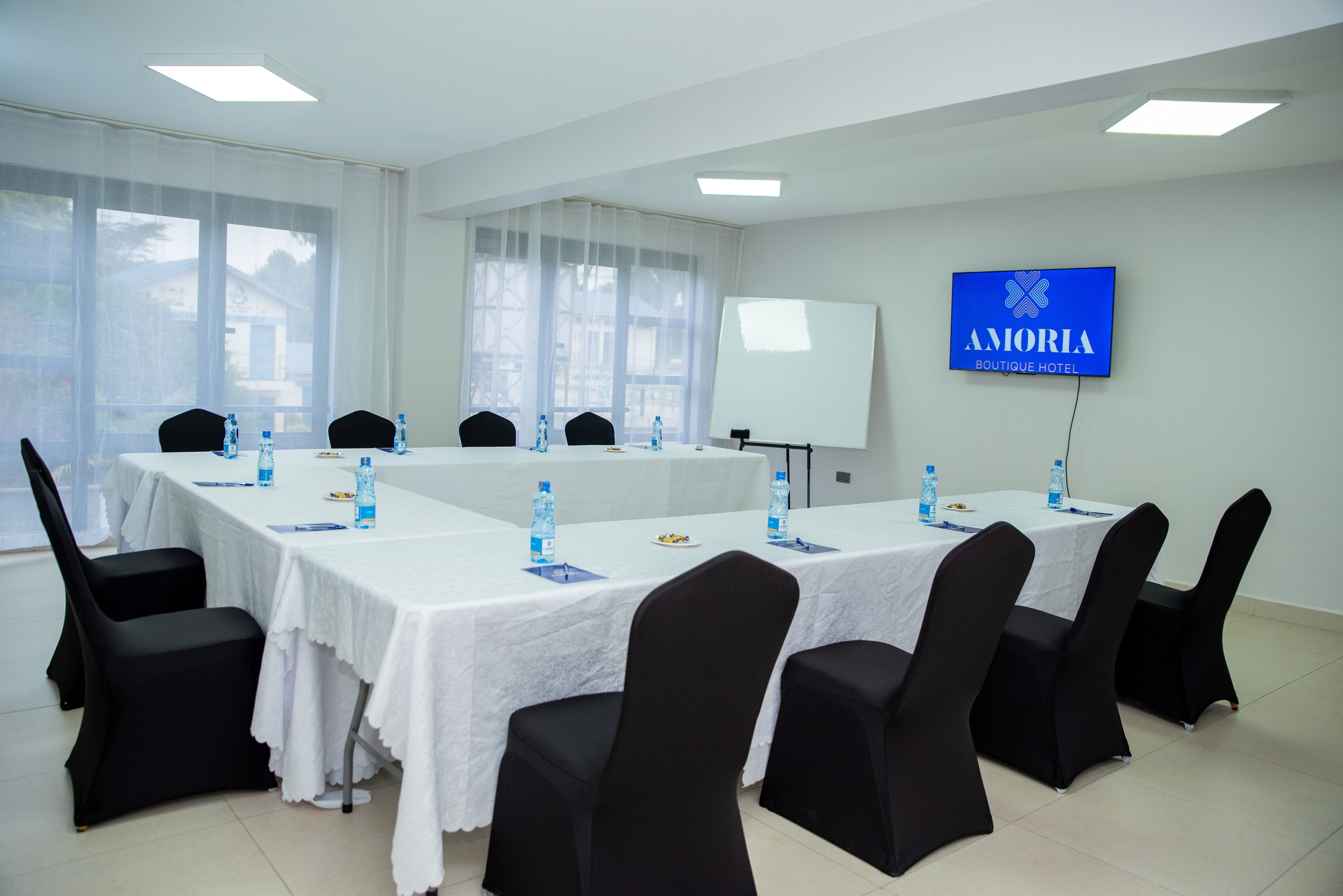 Conference room with white U-shaped tables, black covered chairs, a flipchart and the Amoria wall screen