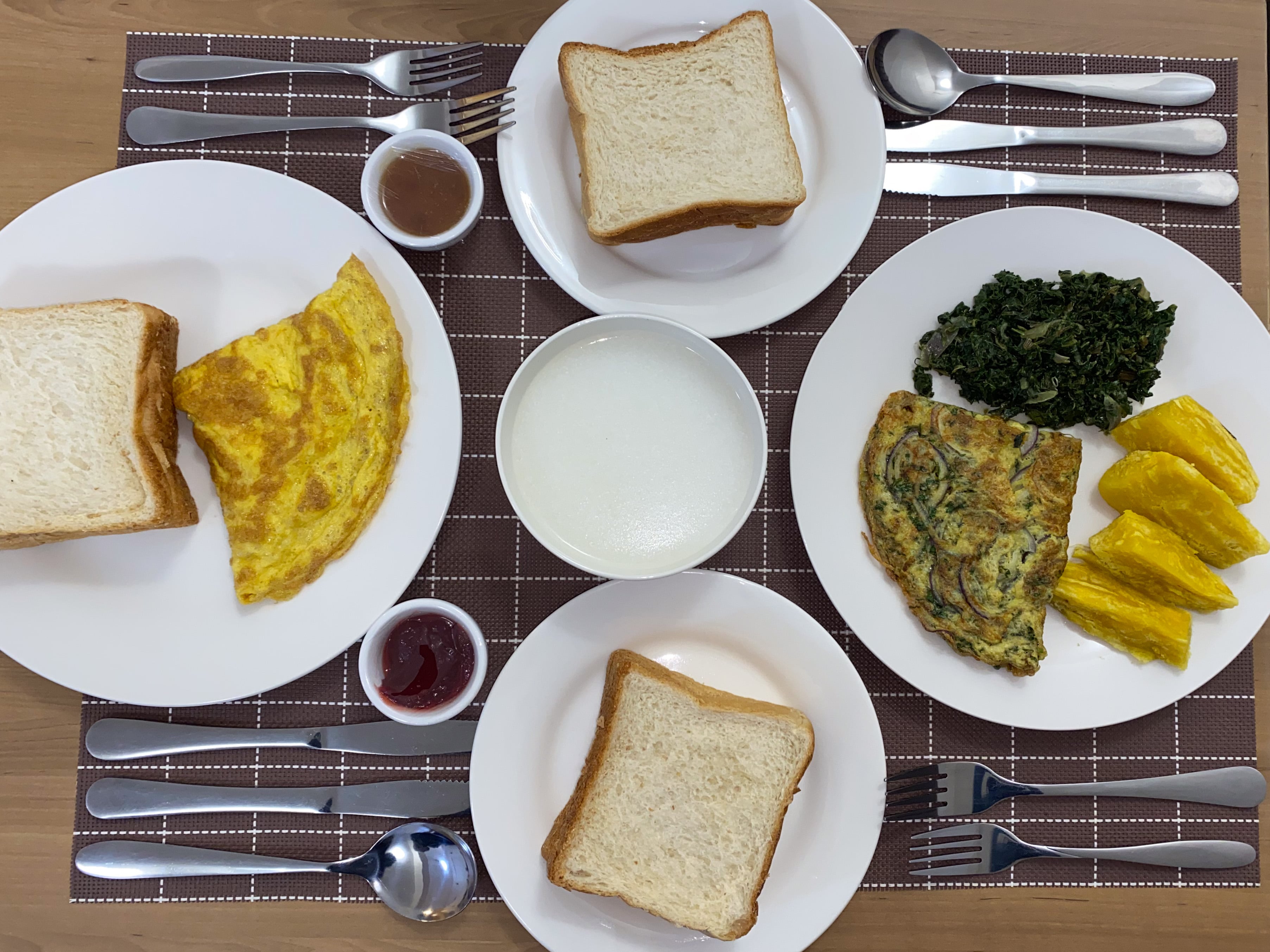 Breakfast for two from above — omelettes, toast, greens, sweet potato and porridge on brown check placemats