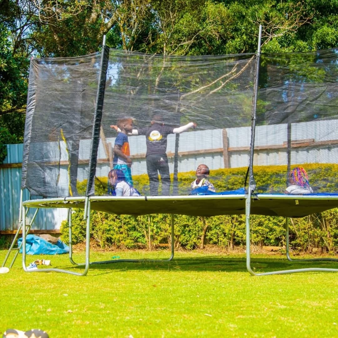 Children bouncing on a netted trampoline at the edge of the lawn