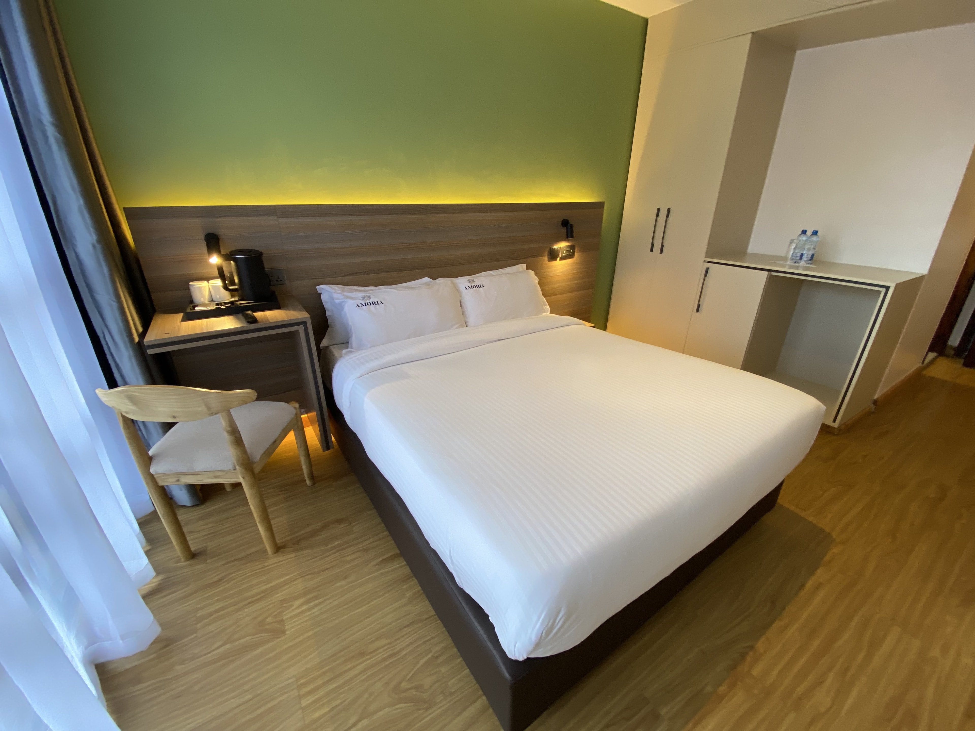 Guest room in daylight with a made double bed, desk chair and kettle station