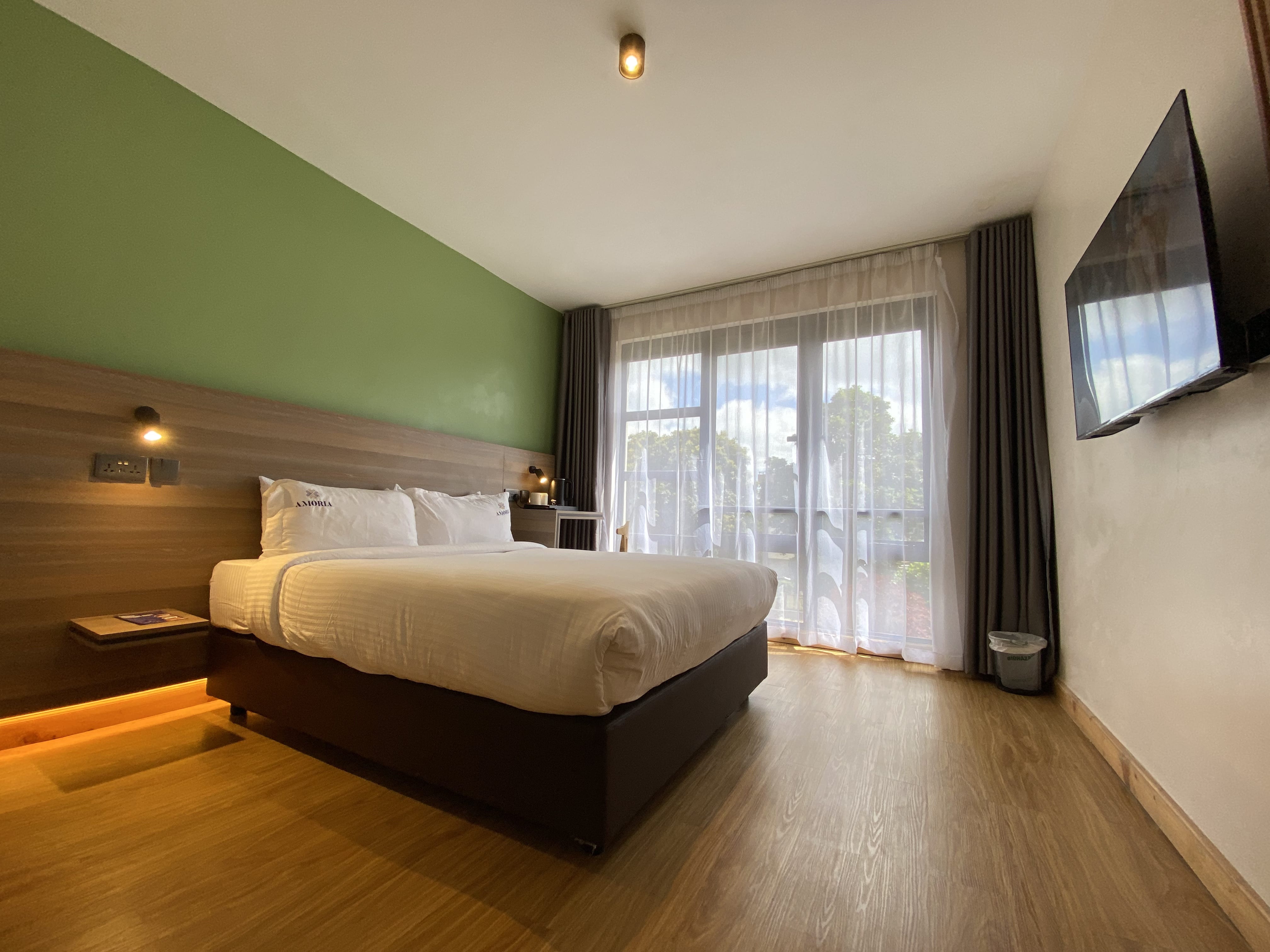 Double bed with Amoria-embroidered pillows beneath the Deluxe room's green feature wall