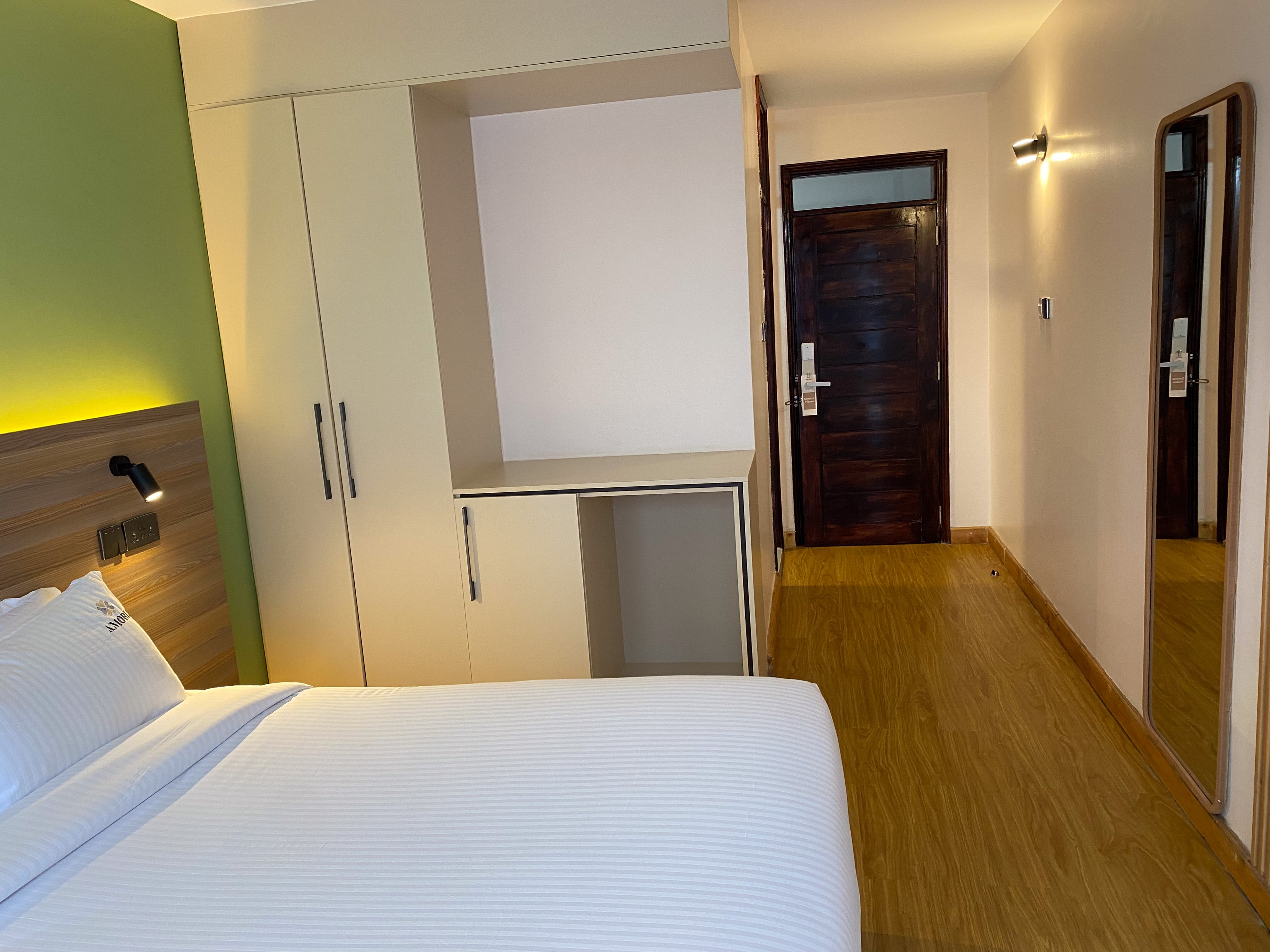 The Standard room from the bed — wardrobe, luggage shelf and the dark-timber entrance door