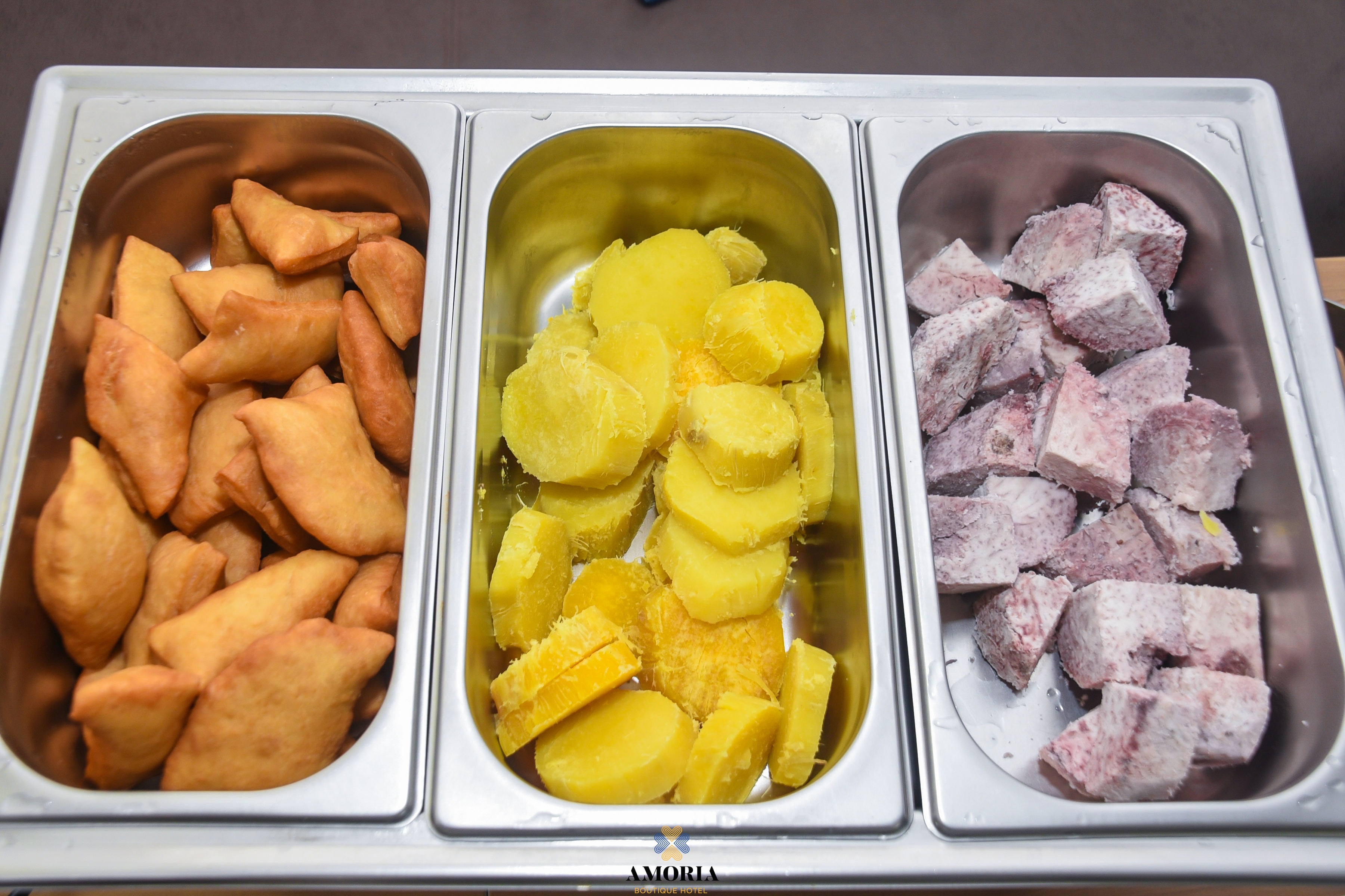 Breakfast buffet trays of golden fried pastries, sliced sweet potato and cubed arrowroot