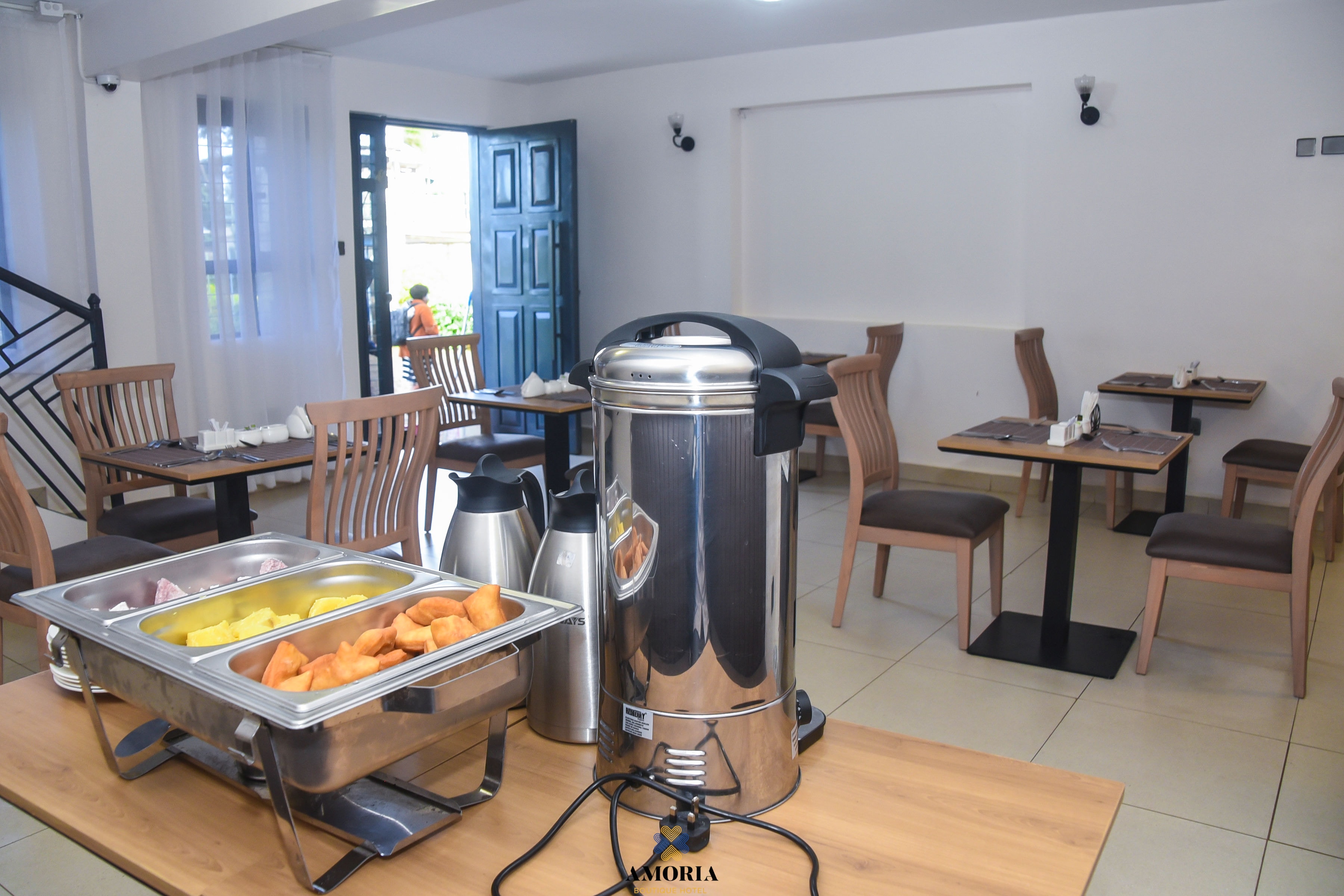 Breakfast room with wooden tables, buffet trays and a hot-water urn
