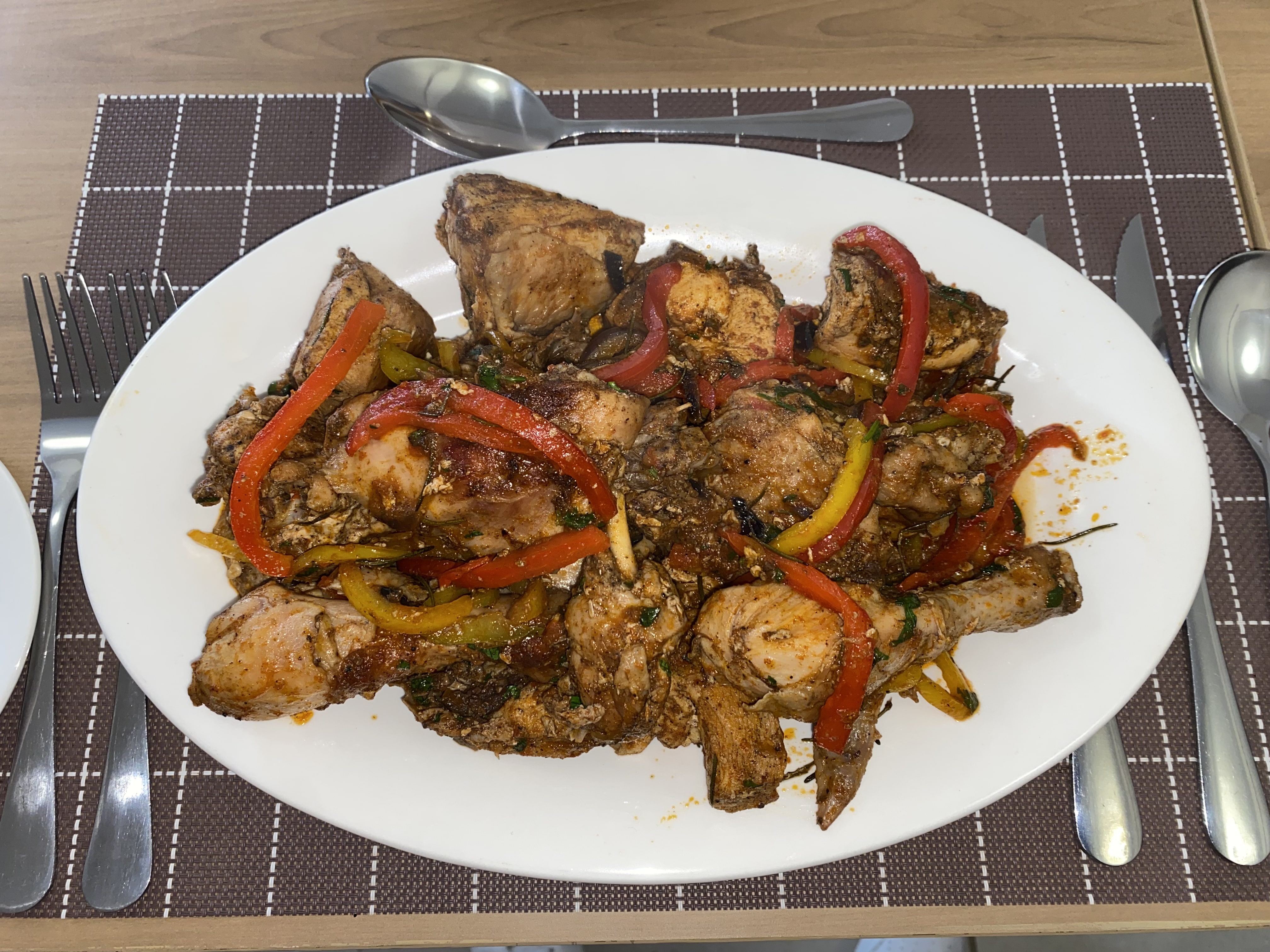 Roast chicken pieces with charred red and yellow peppers on a white sharing platter