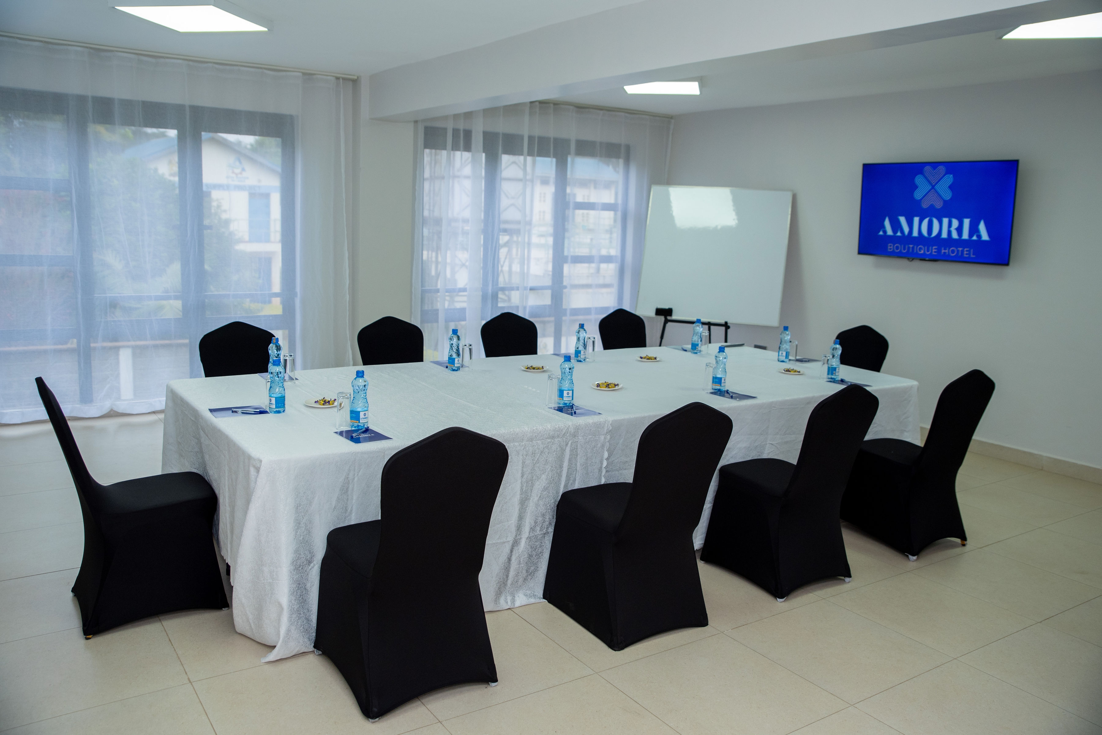 Daylight across white conference tables and black covered chairs, with a flipchart beside the Amoria screen